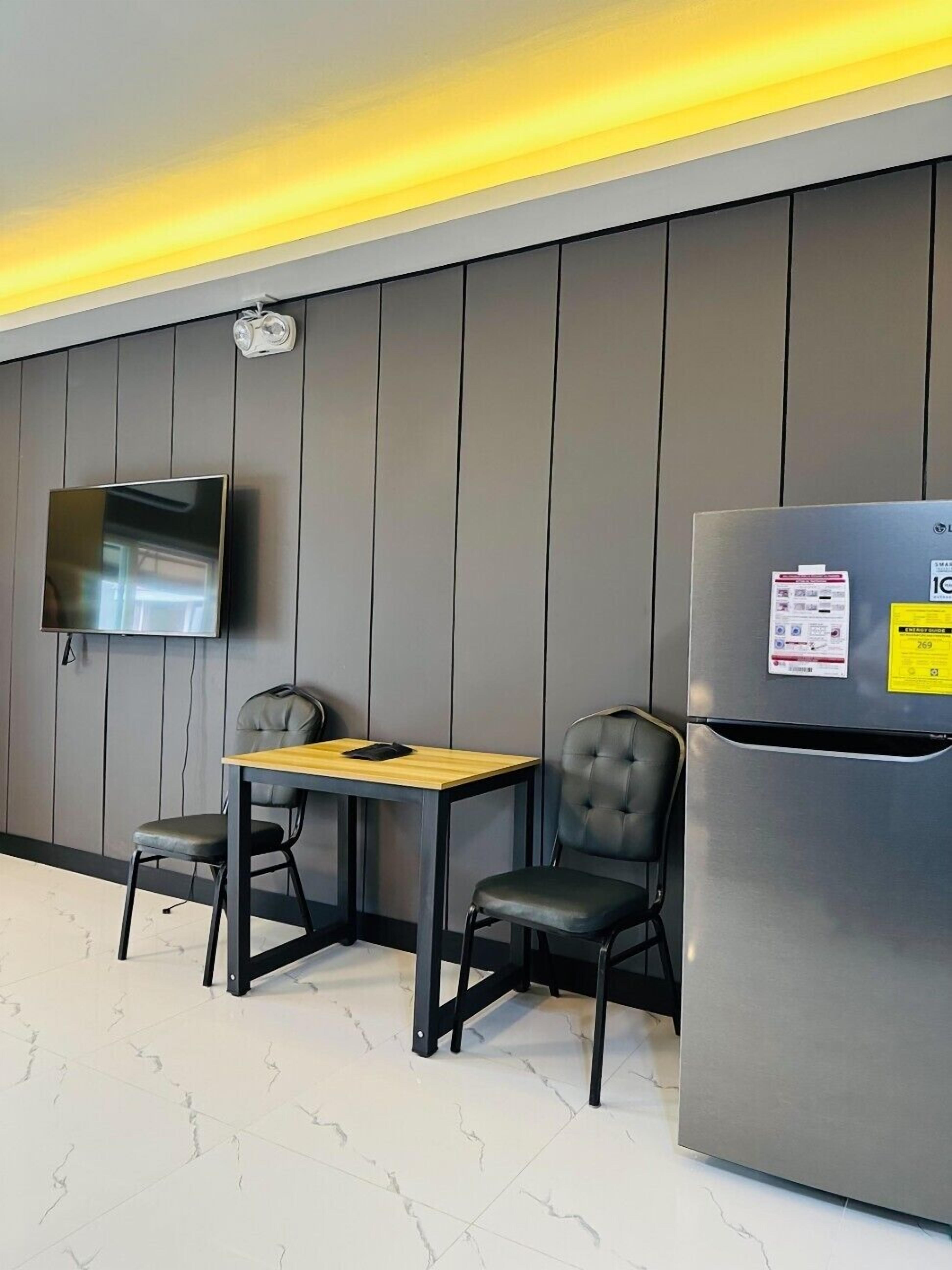 Una cocina moderna con un refrigerador de acero inoxidable, un televisor de pantalla plana montado en la pared y dos sillas negras junto a una mesa de madera.