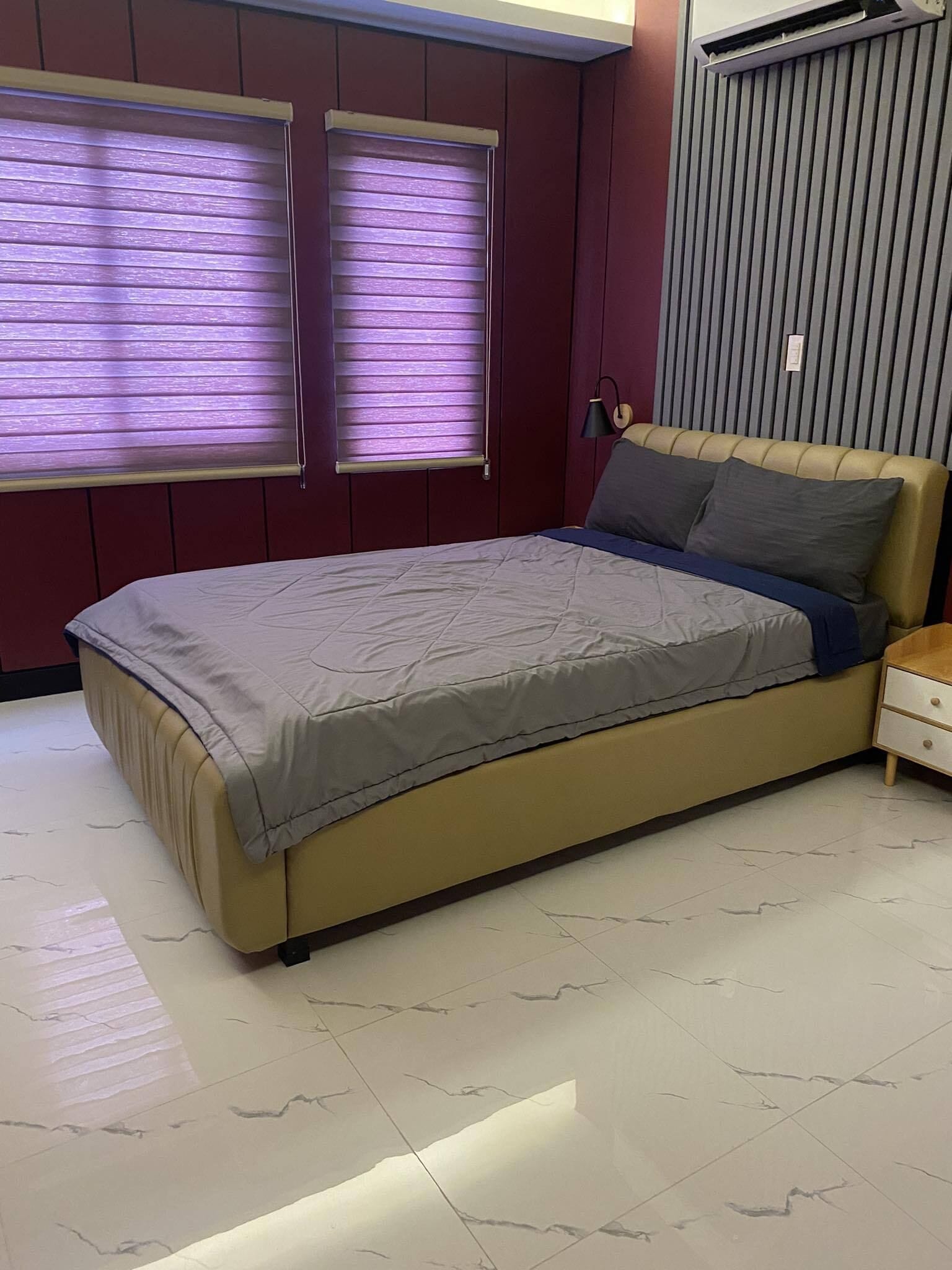A bedroom with a bed, two windows with blinds, a bedside lamp, and a radiator.