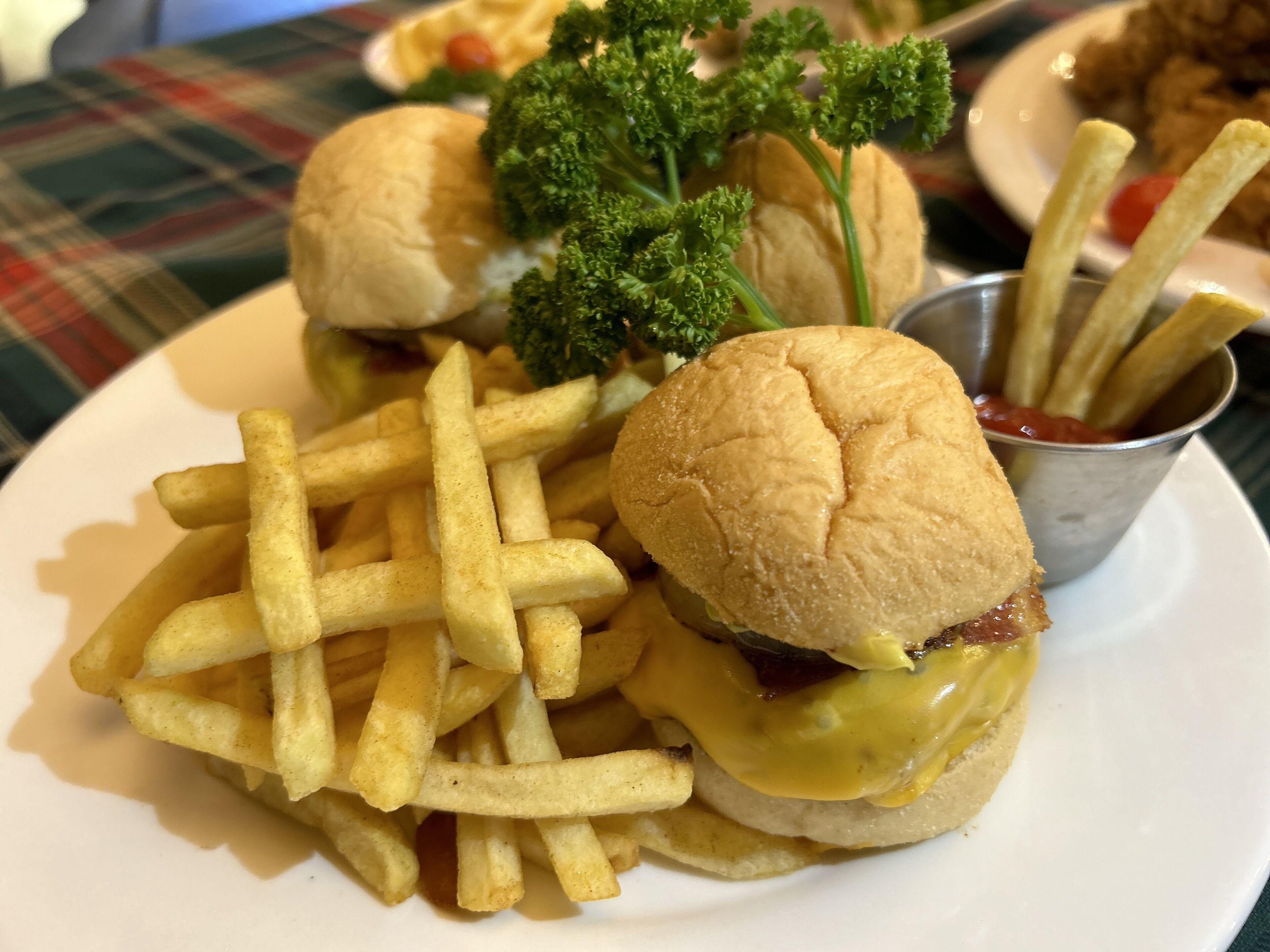 A plate with two burgers, fries, and a small cup of ketchup.