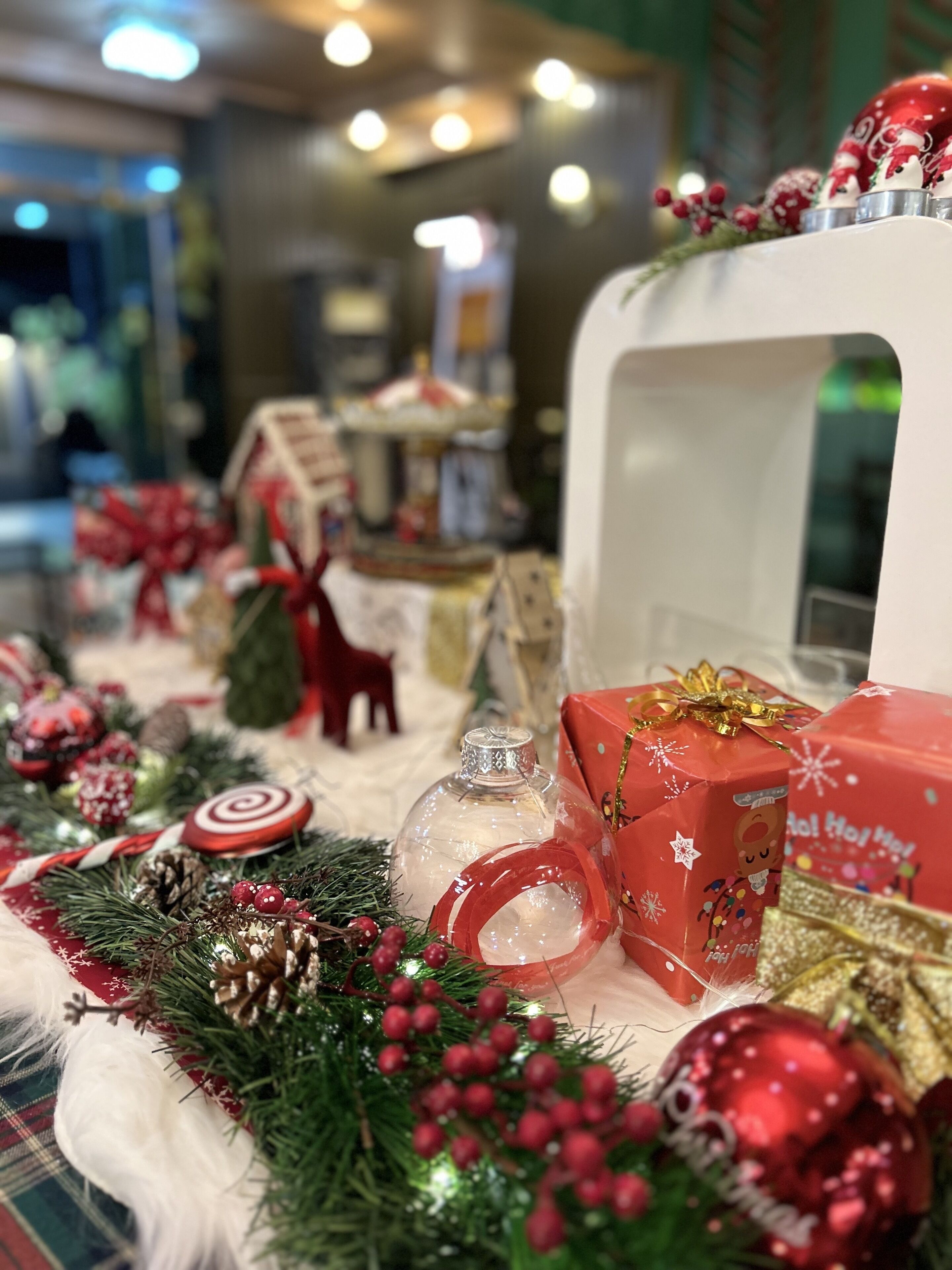 Une décoration festive avec des éléments de Noël, notamment un globe à neige, des cadeaux emballés et une maison en pain d’épices.