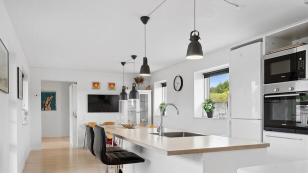 Une cuisine moderne dotée d’un îlot central, de tabourets de bar, de luminaires suspendus et d’appareils électroménagers en acier inoxydable.