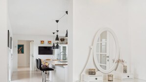 Une pièce moderne et minimaliste, dotée d’une coiffeuse blanche, d’un grand miroir et d’un coin bar avec des tabourets et des luminaires suspendus.