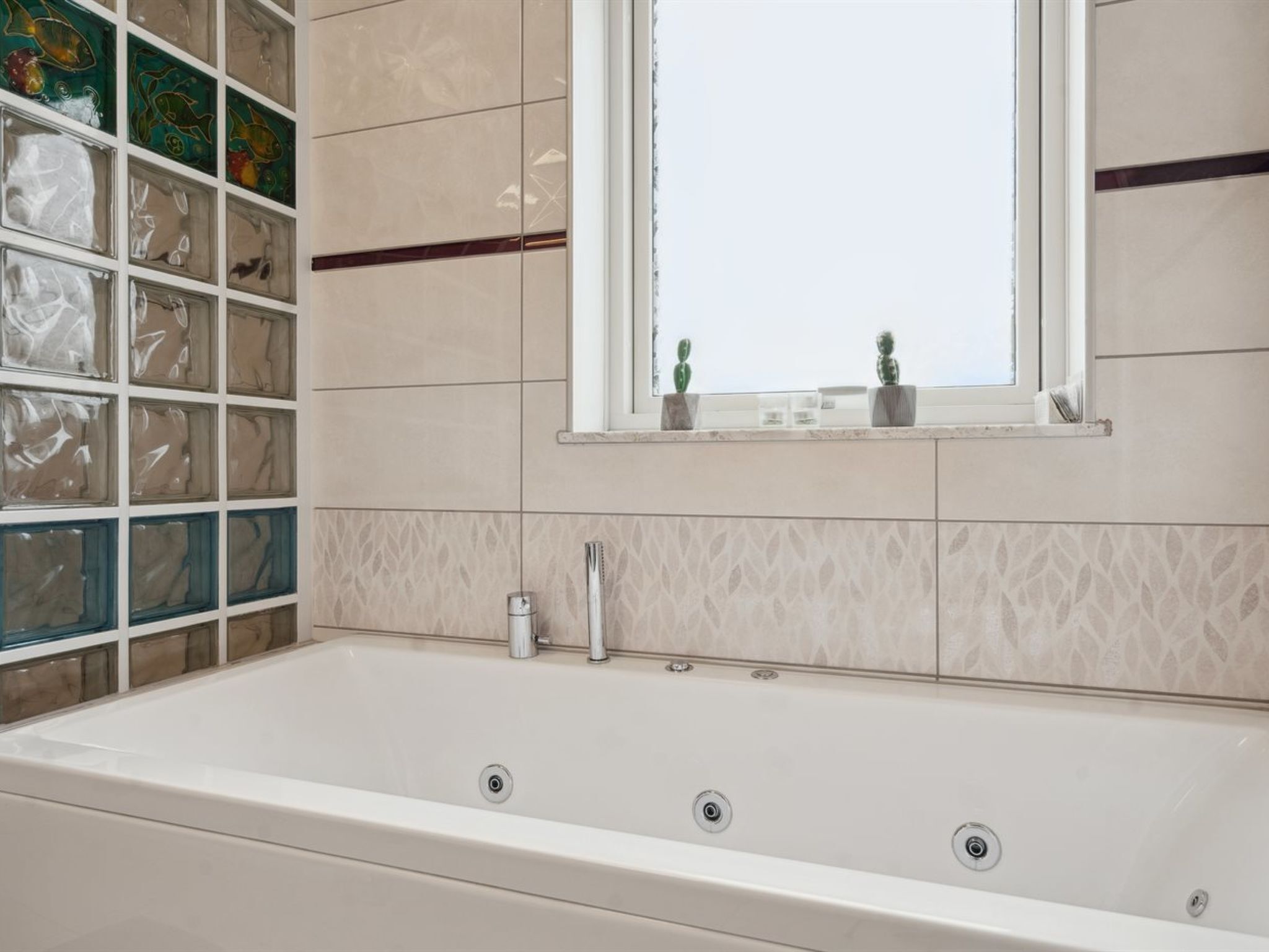Un baño con una bañera grande, una ventana con vistas y una pared decorativa de bloques de vidrio.