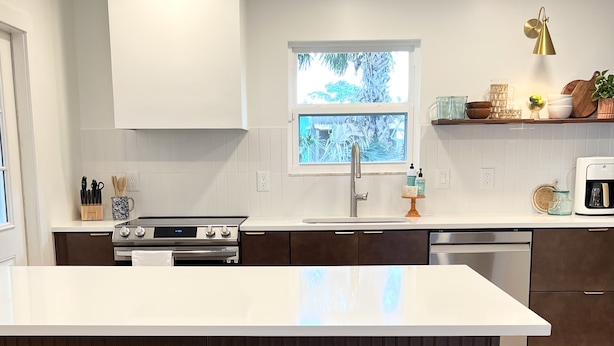 A modern kitchen with a large island, dark cabinetry, and a window with a view.