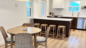 A modern kitchen with a central island, white cabinetry, and a dining area with wicker chairs and a round table.