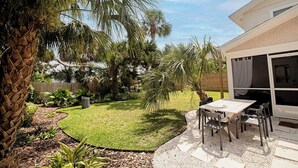 A patio with a table and chairs, surrounded by a well-maintained lawn and palm trees.