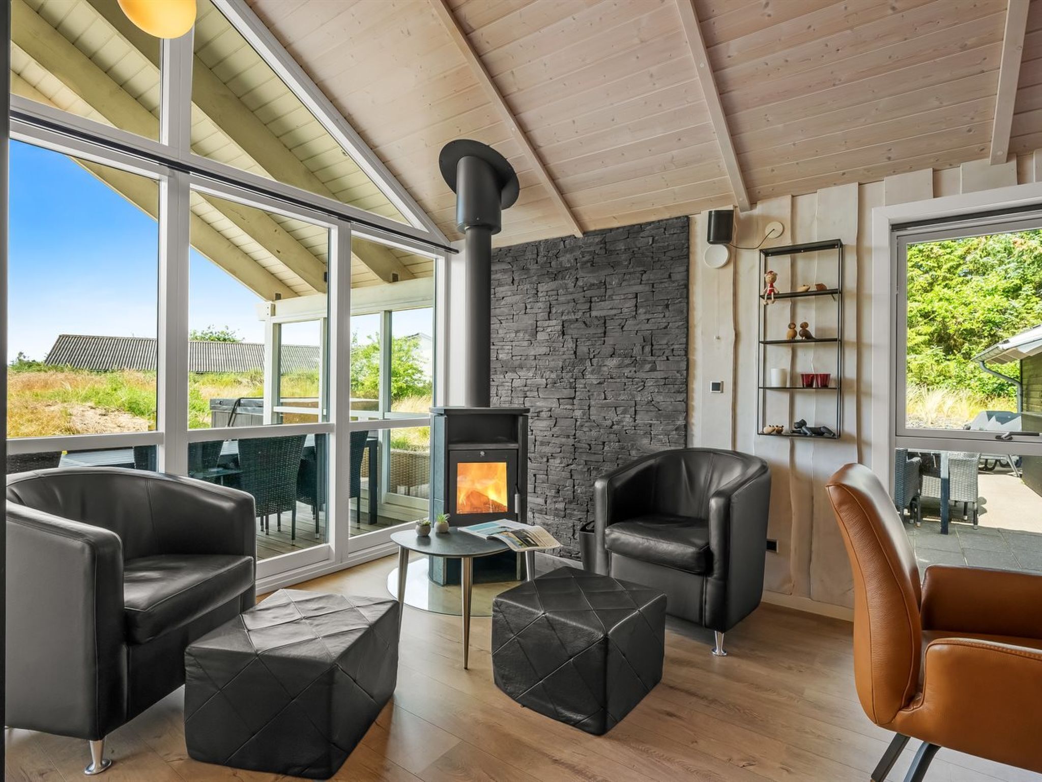 Una sala de estar moderna con chimenea de piedra, muebles de cuero y grandes ventanales con vistas al exterior.