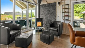 A modern living room with a stone fireplace, leather furniture, and large windows offering a view of the outdoors.