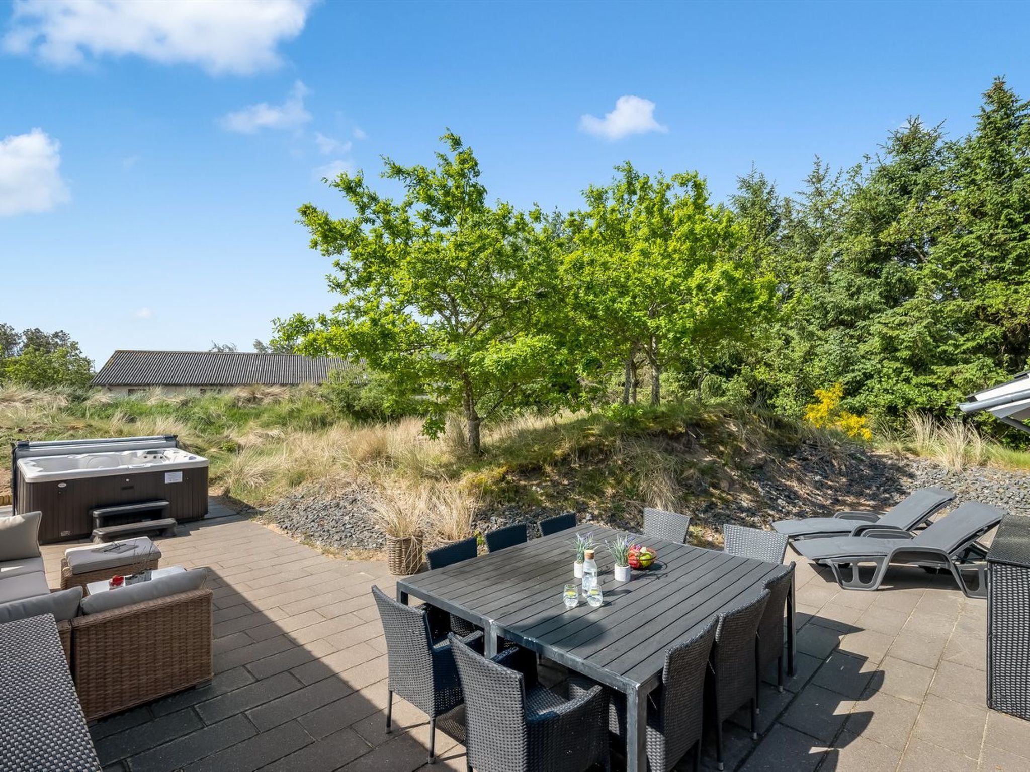 Une terrasse extérieure avec une table et des chaises, un jacuzzi et une pelouse avec des arbres.