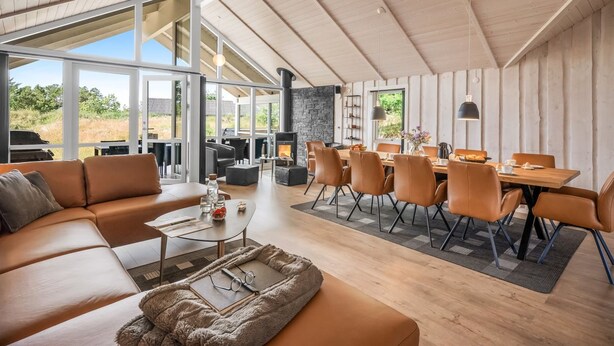 A modern interior with a wooden ceiling, a stone fireplace, leather furniture, and large windows offering a view of the outdoors.