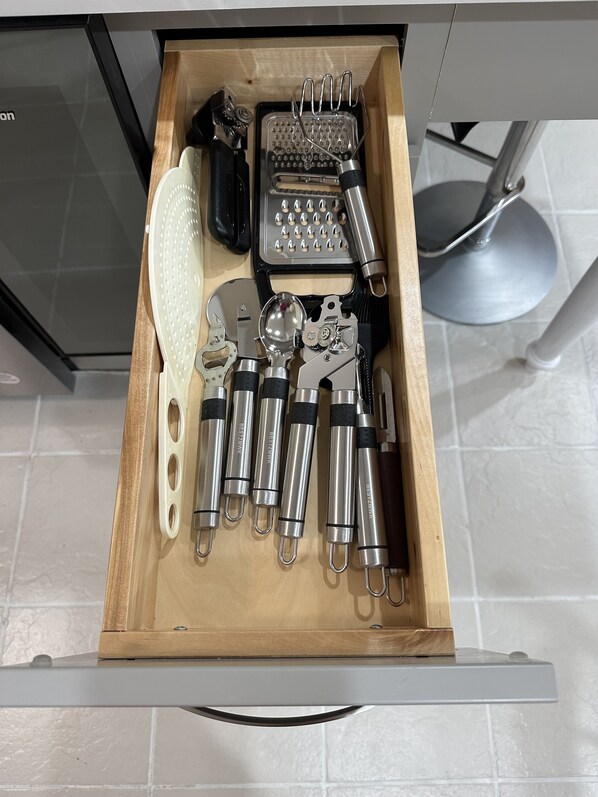 Un cajón con diferentes utensilios de cocina, incluyendo un rallador, un pelador y varias herramientas metálicas.