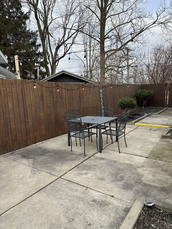 Un patio trasero con mesa y sillas, una cerca de madera y un letrero de bienvenida.