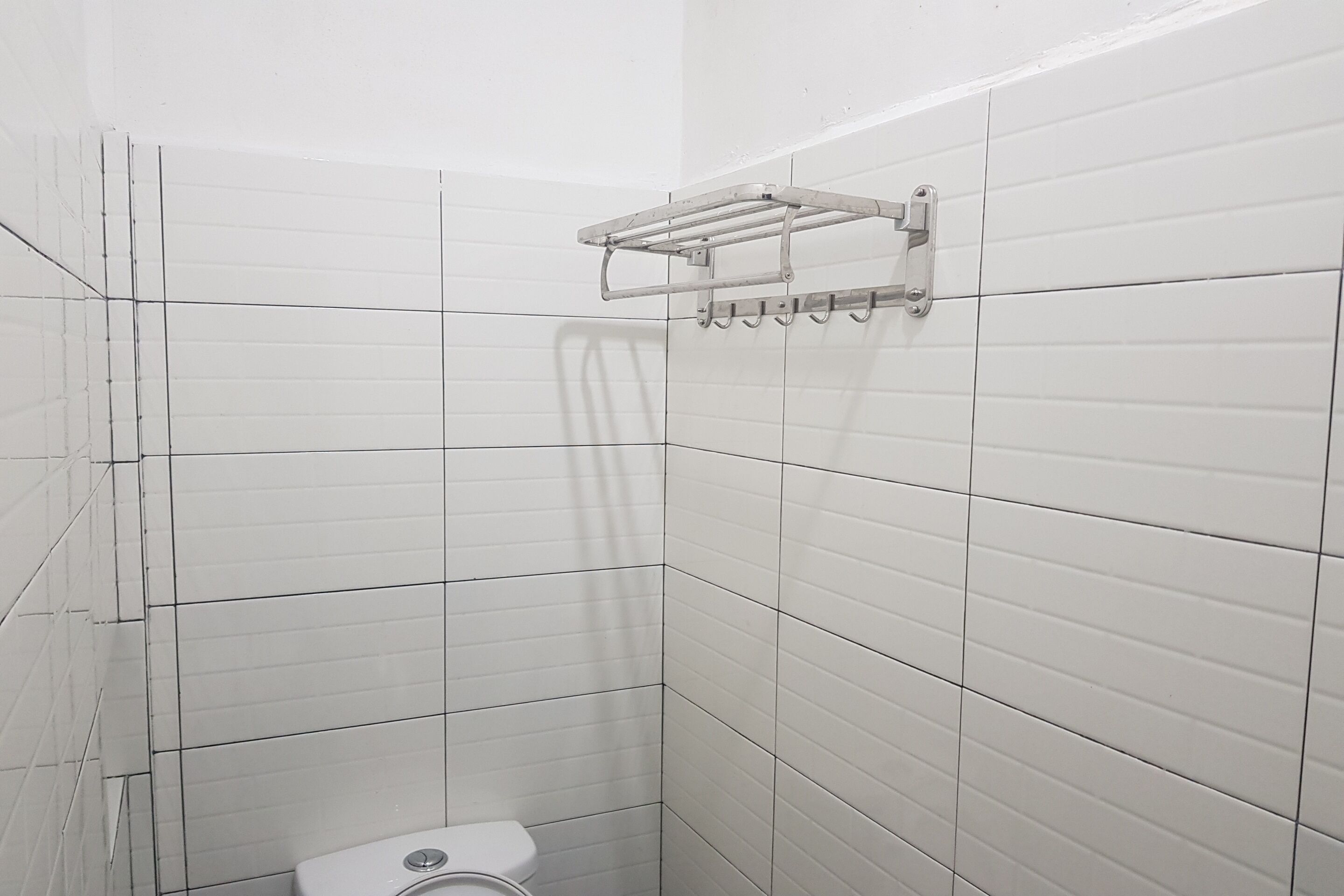 A small, tiled bathroom with a toilet and a metal towel rack.
