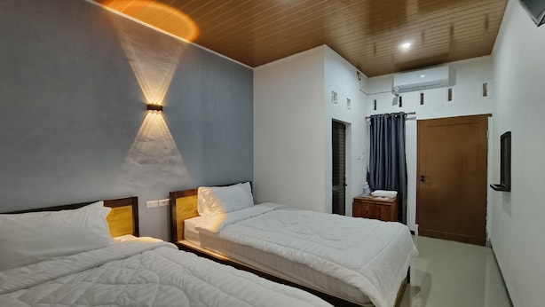A hotel room with two beds, a wooden ceiling, a wall-mounted air conditioner, and a door with a curtain. - OYO 93709 Rose Inn 2 (Medan)