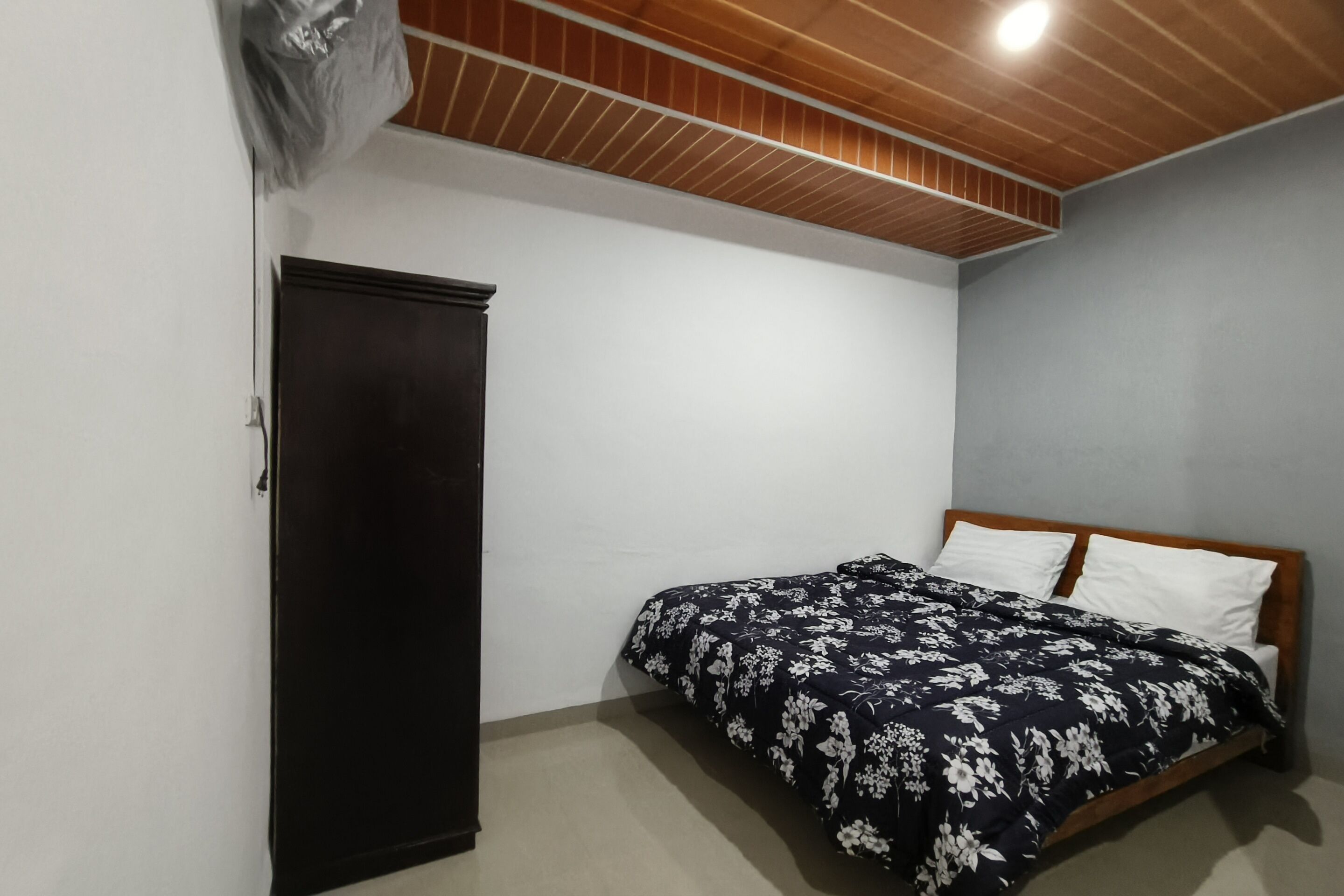 A bedroom with a bed, wooden headboard, and a dark wardrobe.