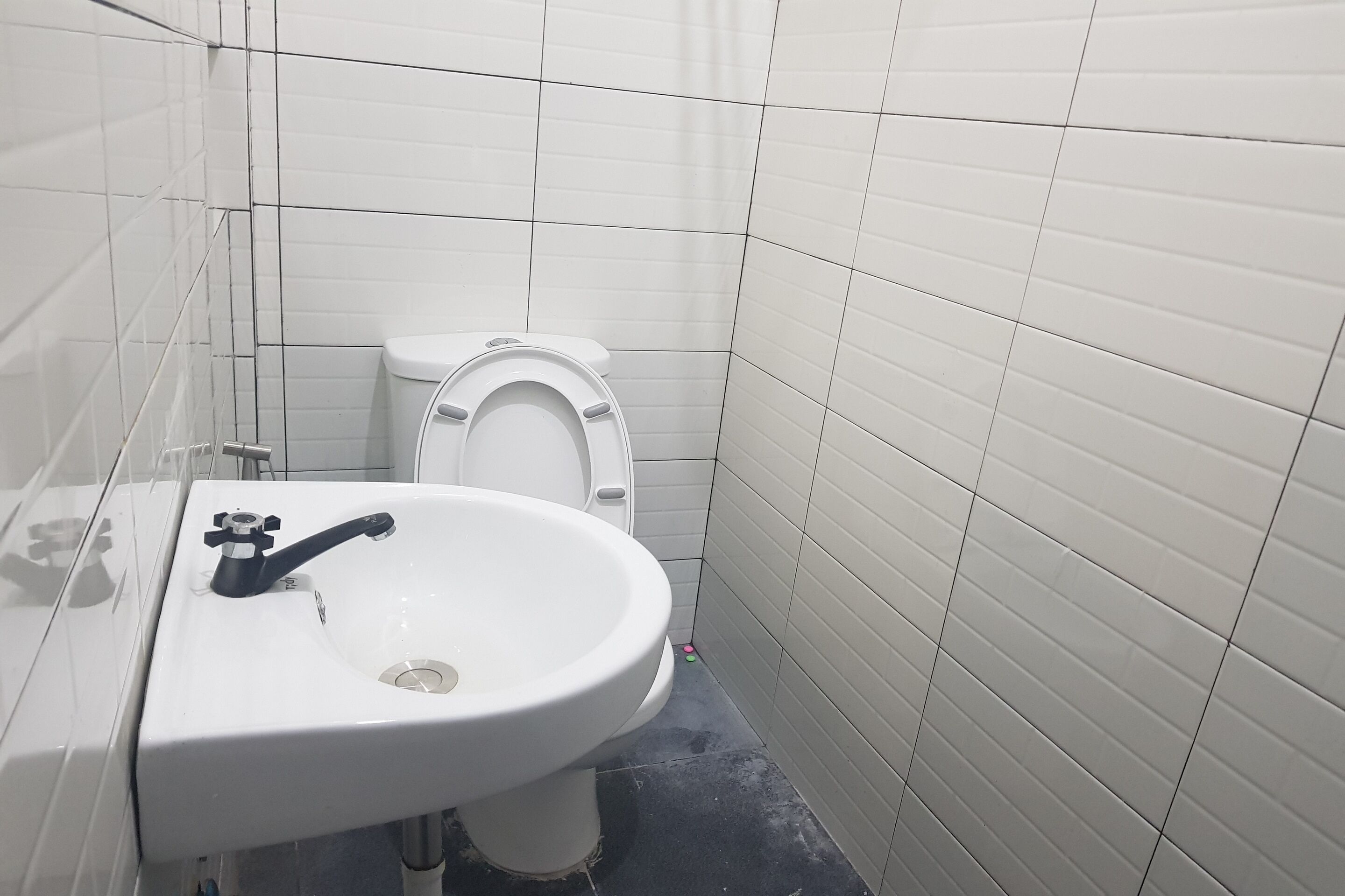 A small, clean bathroom with white tiles, a white sink, and a toilet.