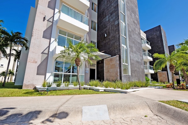 A modern building with a flat roof, large windows, and a paved entrance area with a small garden.