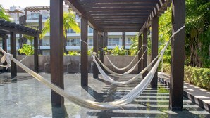 A hammock under a wooden pergola over a pool, with a view of a building and greenery in the background. - MareAzul 705N (Playa del Carmen)