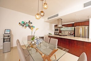 A modern kitchen with stainless steel appliances, a glass dining table, and a water dispenser.