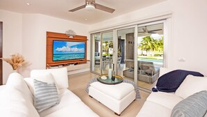 A modern living room with a flat-screen TV, a ceiling fan, and a glass door leading to a pool area. - MareAzul 705N (Playa del Carmen)