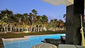 A pool area with lounge chairs and pillows, surrounded by palm trees and a clear sky. - MareAzul 705N (Playa del Carmen)