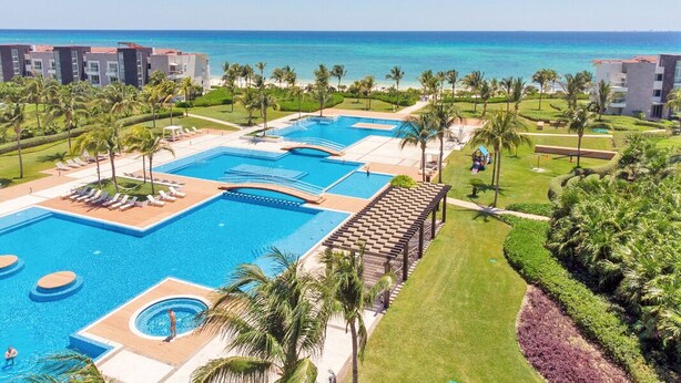 A resort with multiple swimming pools, palm trees, and a view of the ocean. - MareAzul 705N (Playa del Carmen)