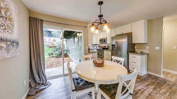 A modern kitchen with white cabinets, a central island, and a dining area with a round table and chairs. - Storybook Tacoma Cottage Escape (Tacoma)