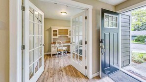 A hallway with a wooden floor, a desk with a chair, and a door leading outside. - Storybook Tacoma Cottage Escape (Tacoma)