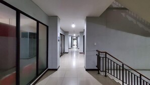 A long, narrow hallway with a staircase on the right, leading to an upper floor. The walls are plain with a light color, and the floor is tiled. - Collection O 93708 Tamansari Panoramic Apartment By Rasya Rooms (Bandung)