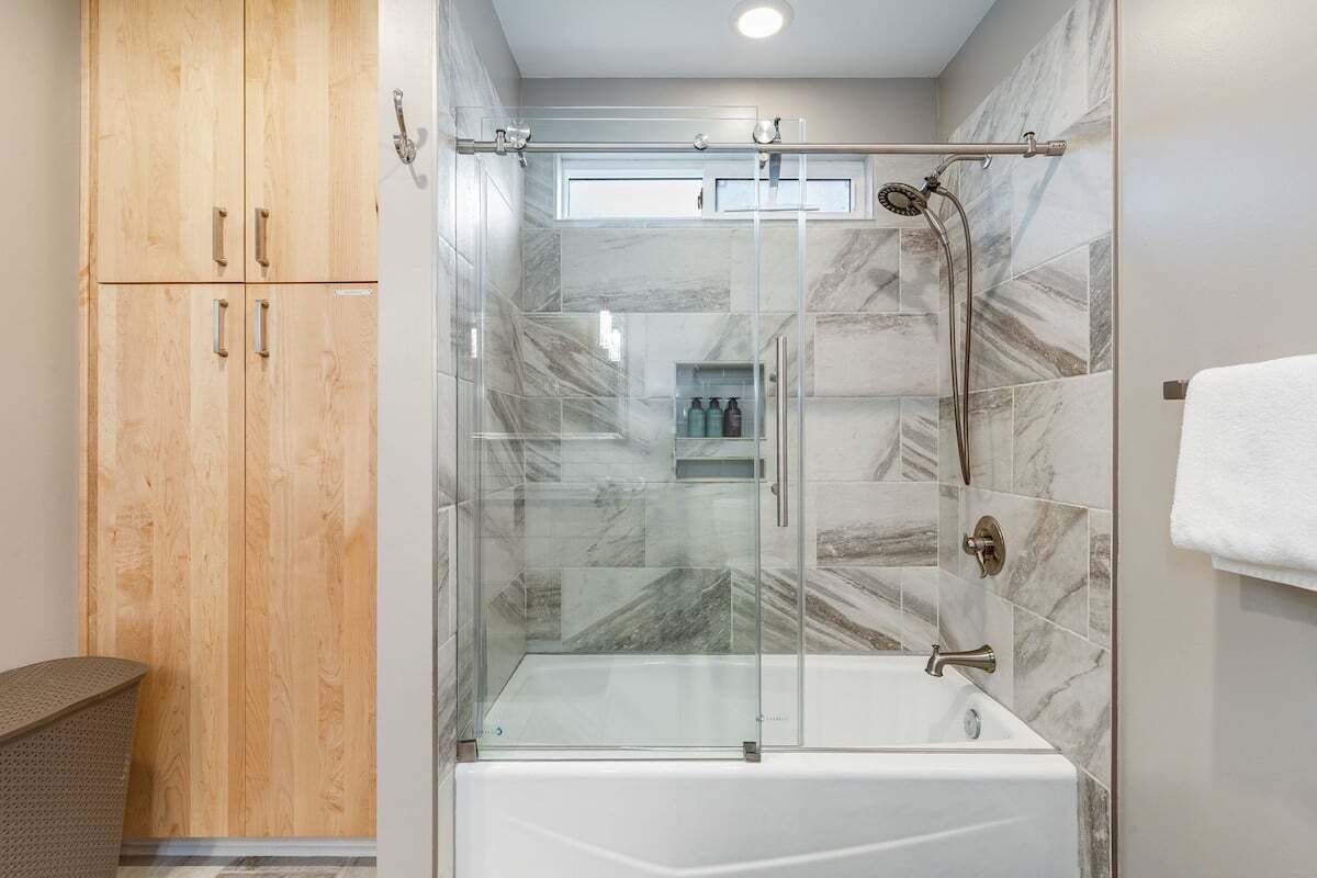 A modern bathroom with a glass-enclosed shower, a white bathtub, and wooden cabinets.