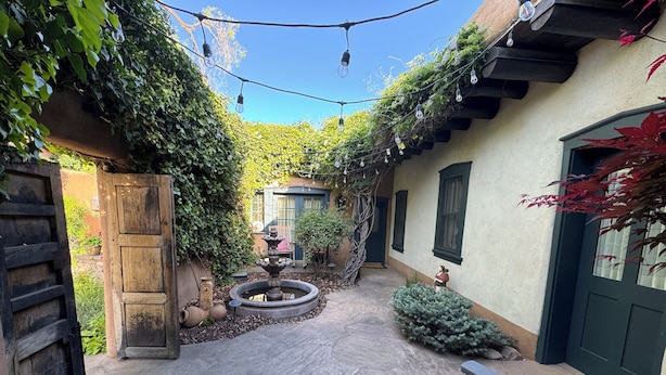 Une cour avec une fontaine, deux fauteuils Adirondack et un portail en bois.
