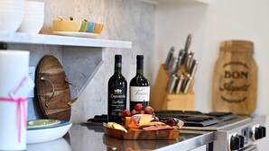 Un comptoir de cuisine avec deux bouteilles de vin, un saladier de fruits et une planche à découper en bois.