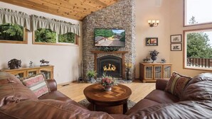 A cozy living room with a stone fireplace, leather sofas, and a television mounted on the wall. - Majestic Sequim Vacation Home near Sequim Bay (Sequim)