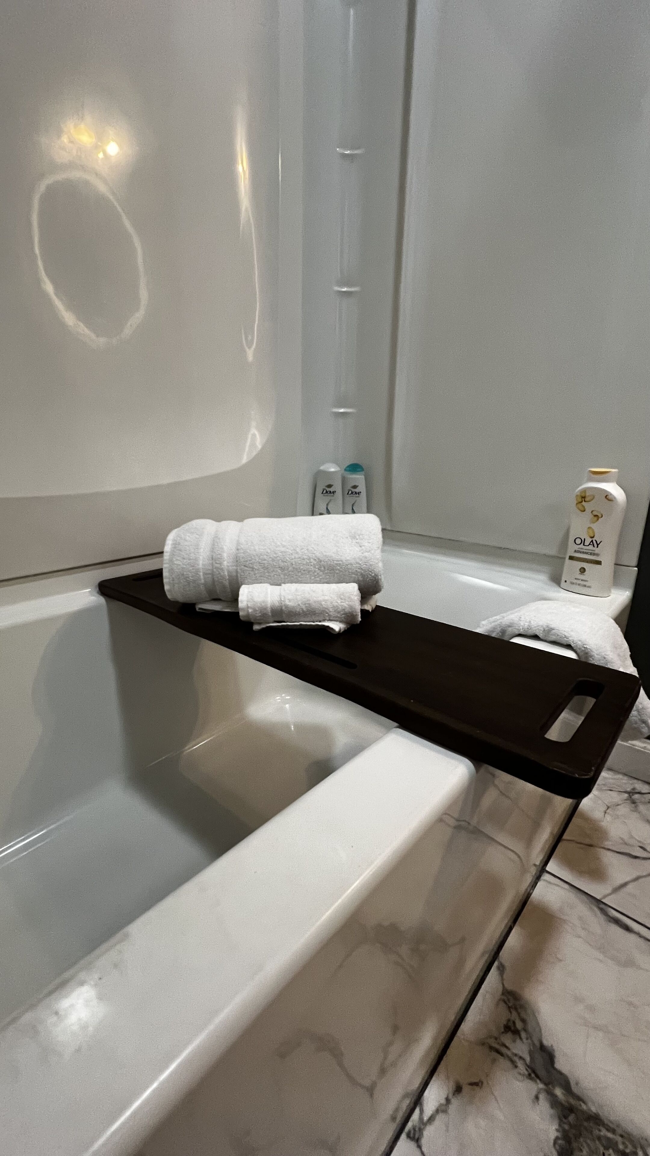 Une salle de bain avec une baignoire, un porte-serviettes avec deux serviettes et deux produits de soins corporels Dove accrochés au mur.