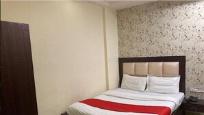 Una cama bien hecha con una colcha roja y blanca, un cabecero de madera y un estampado floral en la pared.