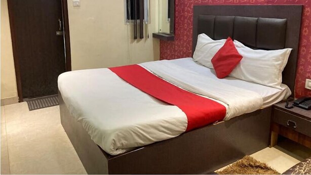 Una cama bien hecha con ropa de cama blanca y roja, un cabecero oscuro y una mesita de noche con un teléfono.