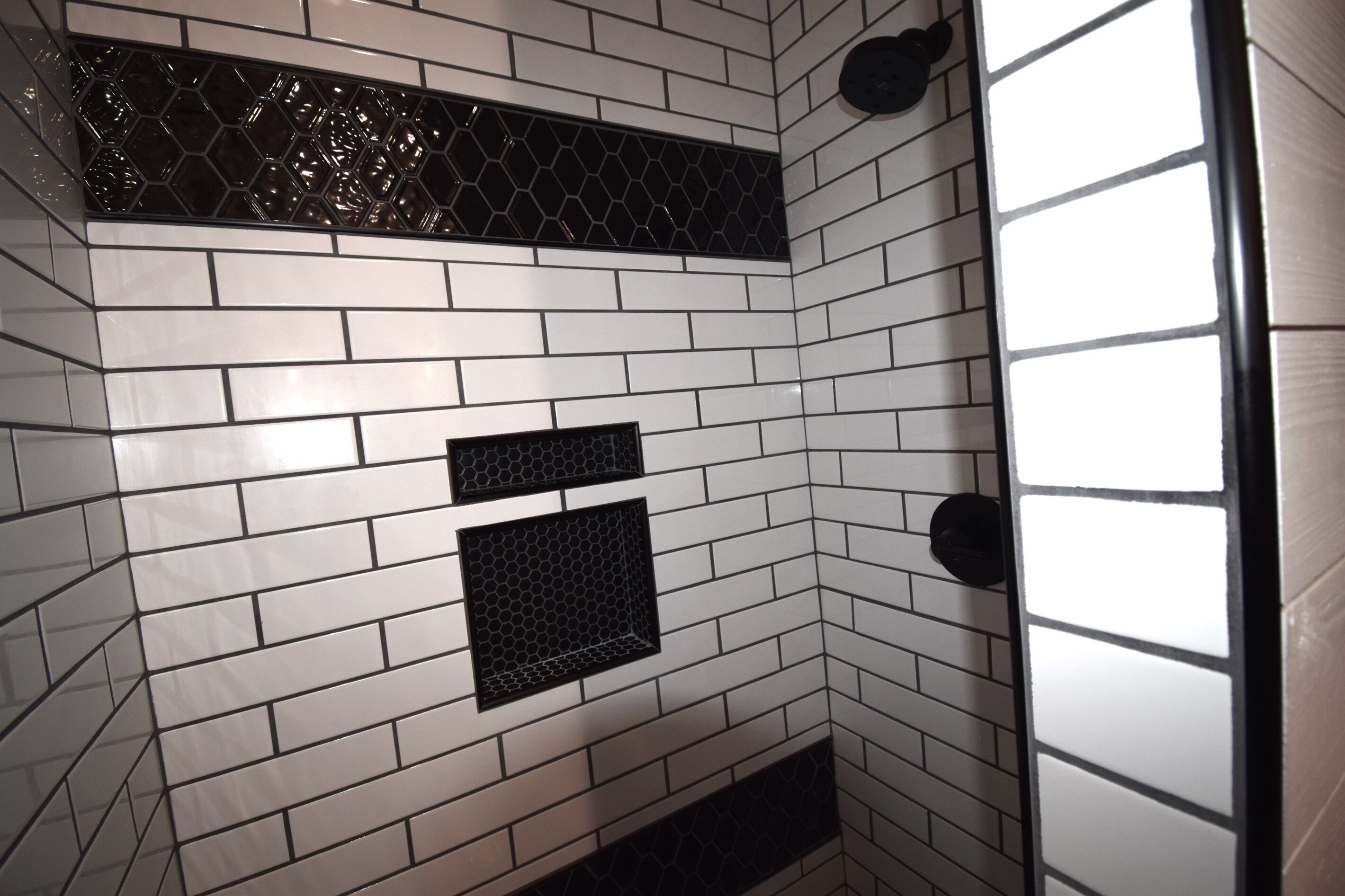 Esquina de una habitación con paredes de azulejos blancos y rejillas hexagonales negras.