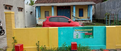 A red car parked in front of a house with a blue door and a signboard on the wall.