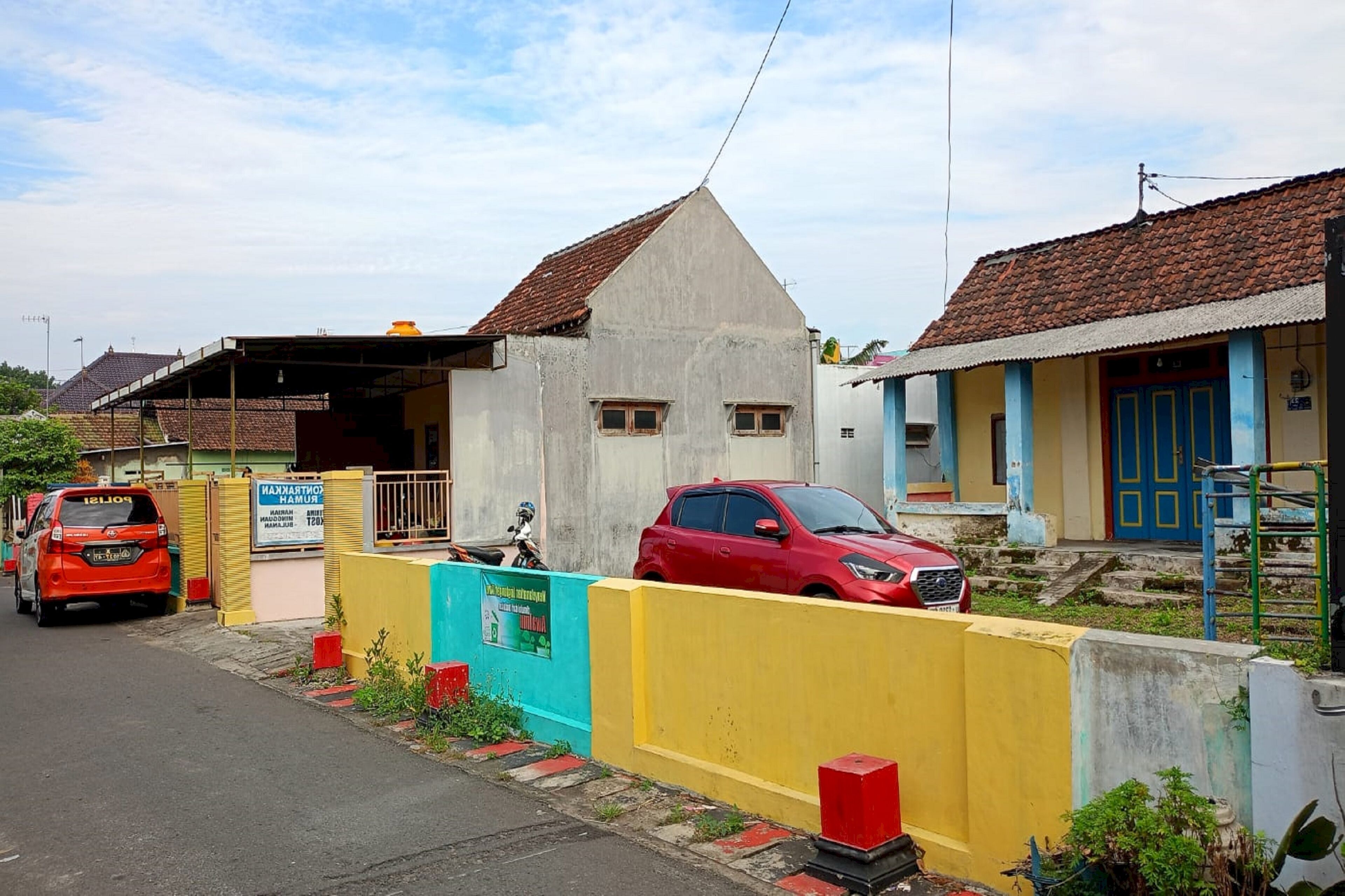 A residential area with a red car parked in front of a house with a blue door.
