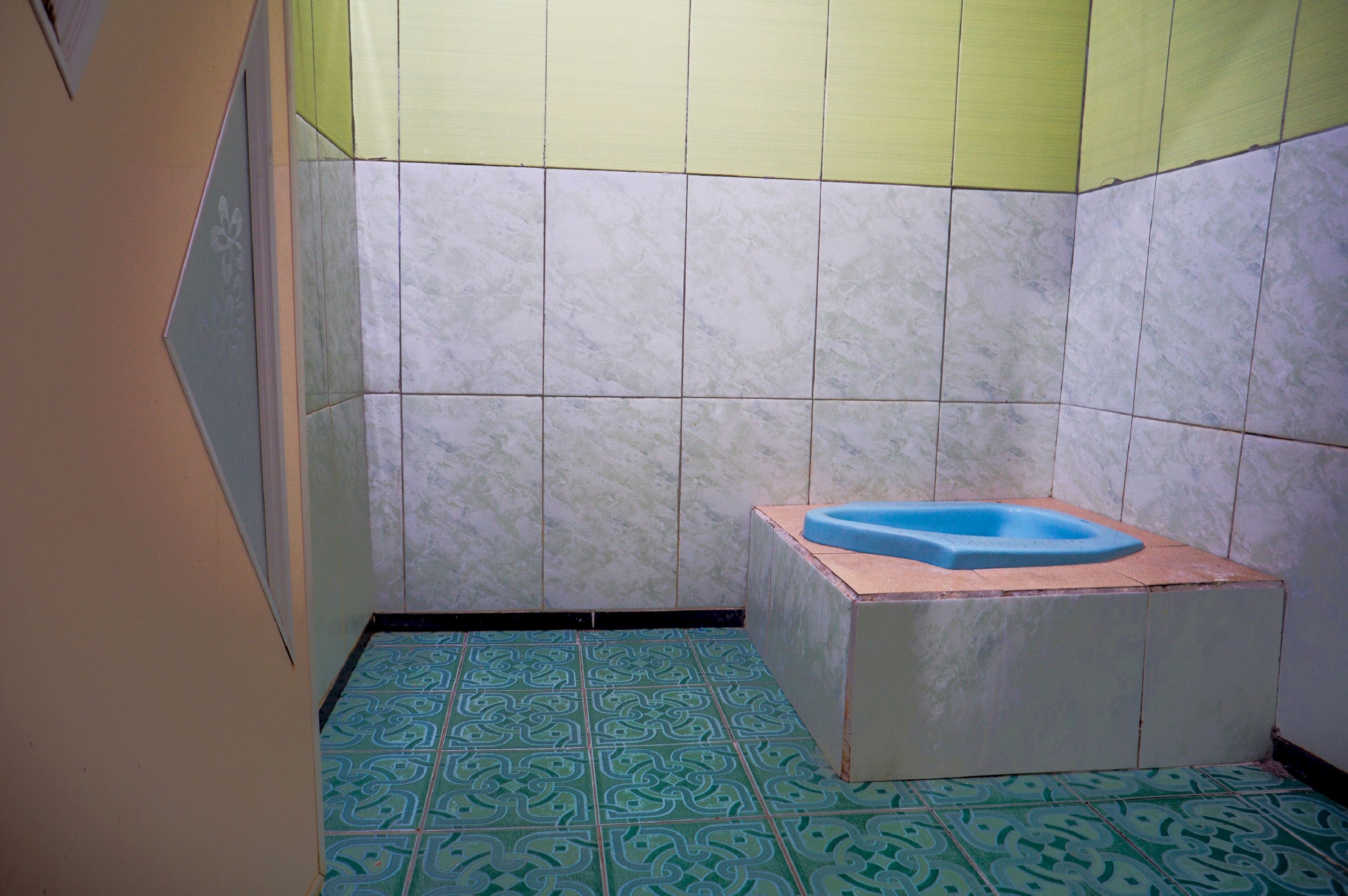 A bathroom with a blue bathtub, patterned floor tiles, and a wall with a geometric design.