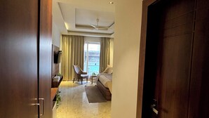 A hotel room with a bed, a sofa, a TV, a desk, and a window with curtains. - Vyom Boutique Hotel (Narendranagar)