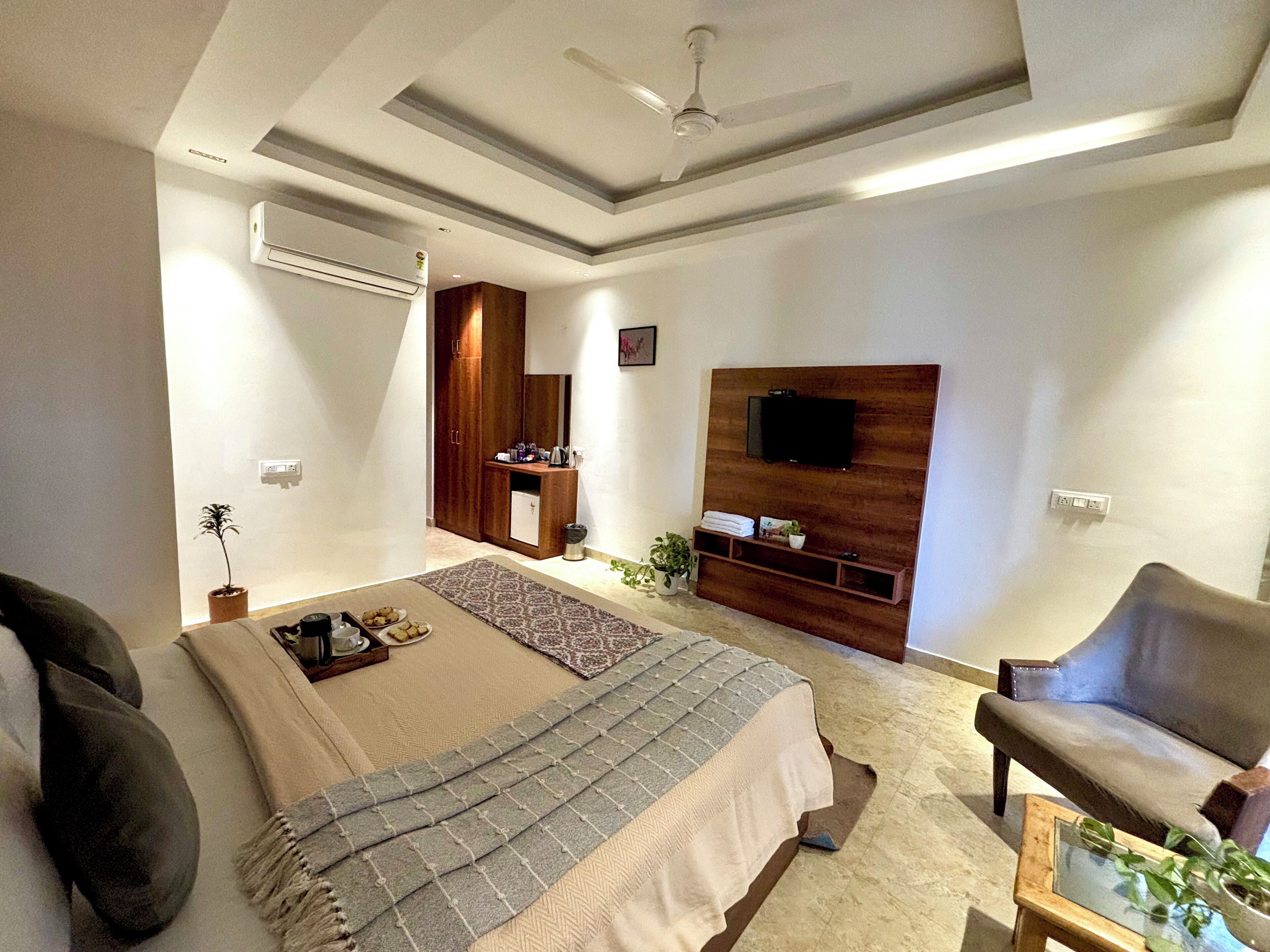 A modern bedroom with a bed, a TV mounted on the wall, a ceiling fan, and a small seating area with a chair and table.