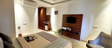 A modern bedroom with a bed, a TV mounted on the wall, a ceiling fan, and a small seating area with a chair and table.