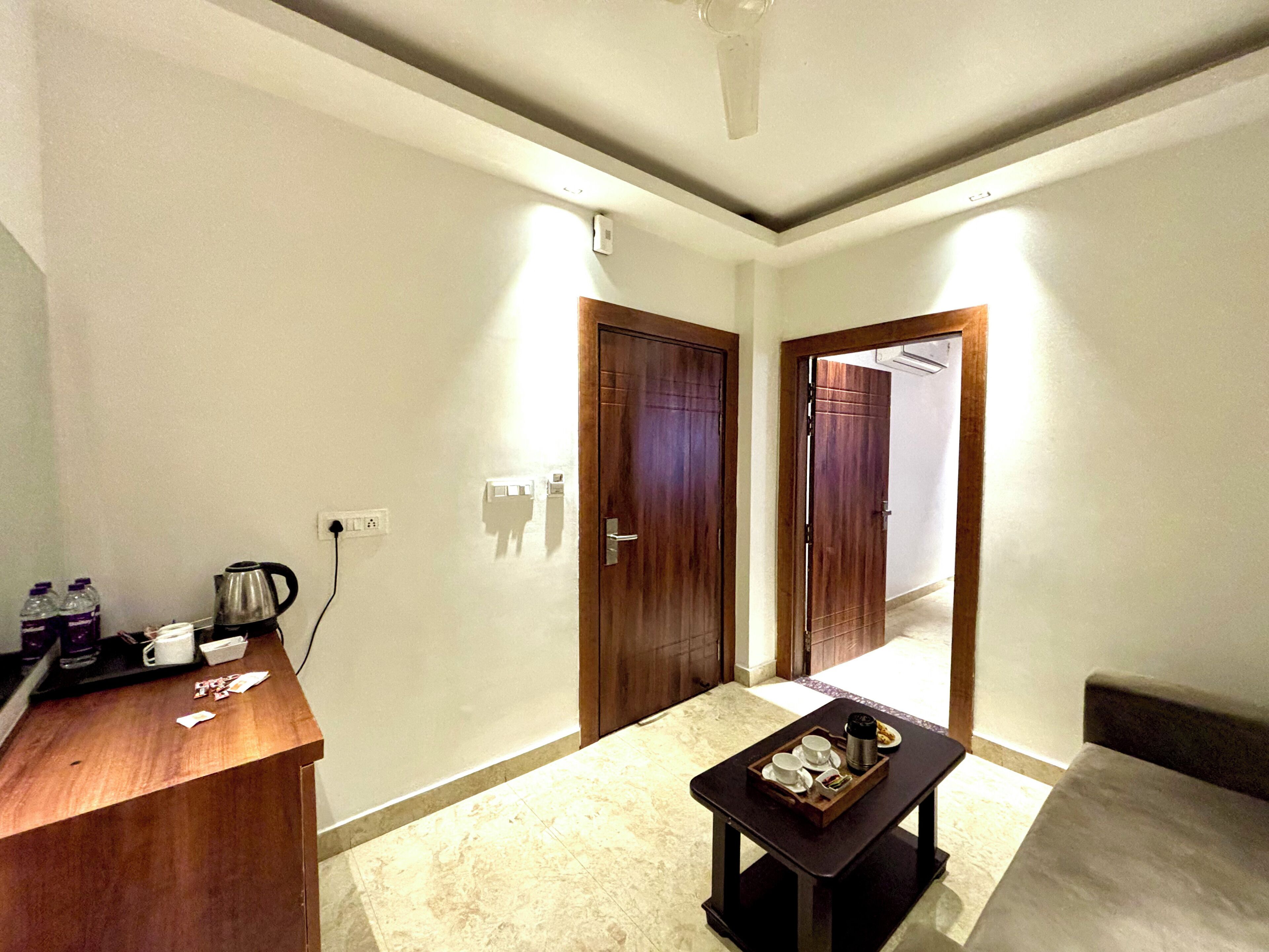 A hotel room with a wooden desk, a coffee maker, and a tray with cups and a teapot. There are two doors, one leading to a hallway and the other to another room.