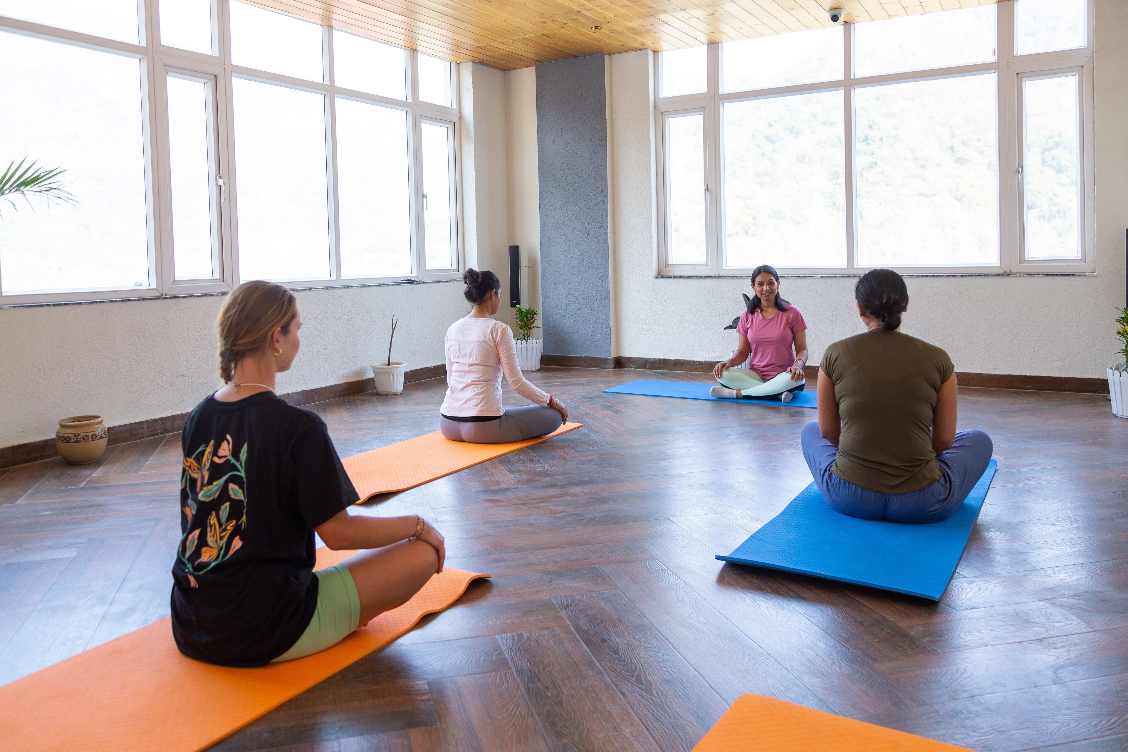 Una clase de yoga en una habitación con ventanas amplias y suelos de madera.