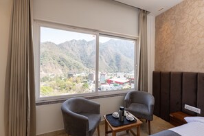 A hotel room with two armchairs, a small table with a tray, a bed, and a large window offering a mountain view.