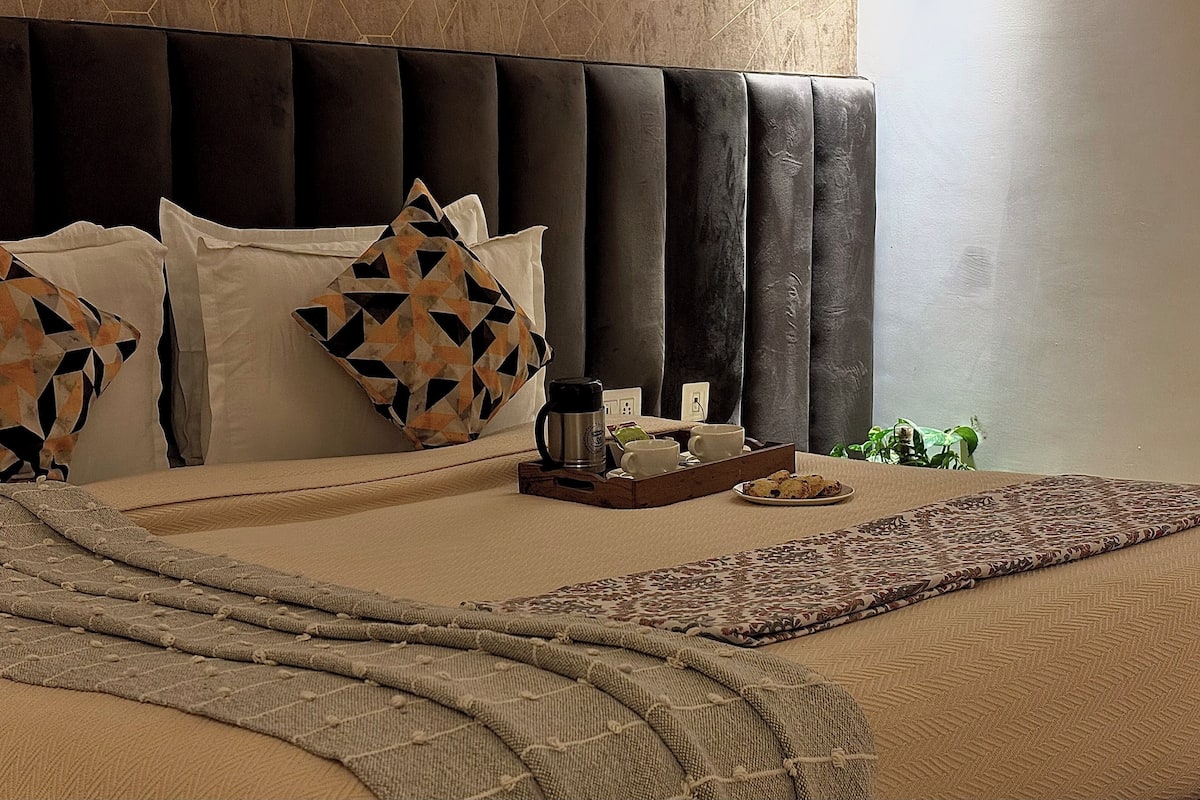Een netjes opgemaakt bed met een bedsprei met patroon, een dienblad met ontbijtartikelen en een potplant.