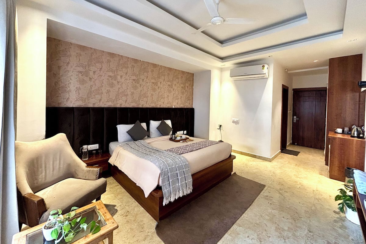 Een moderne slaapkamer met een groot bed, een plafondventilator, een airconditioning, een nachtkastje, een stoel en een bijzettafeltje met een plant.