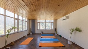A spacious room with wooden ceiling and large windows, featuring yoga mats and potted plants. - Vyom Boutique Hotel (Narendranagar)
