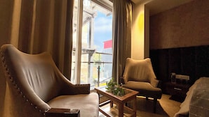 A living room with two leather armchairs, a wooden coffee table, and a view of the city through large windows. - Vyom Boutique Hotel (Narendranagar)